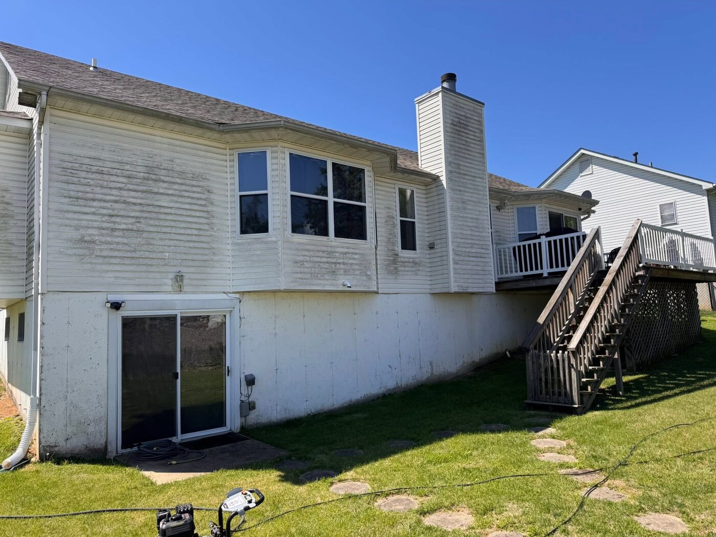 Back of a two-storey home with siding streaked green and grey from algae before washing