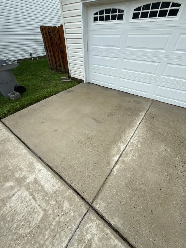 Wide concrete driveway in front of a white garage door after cleaning